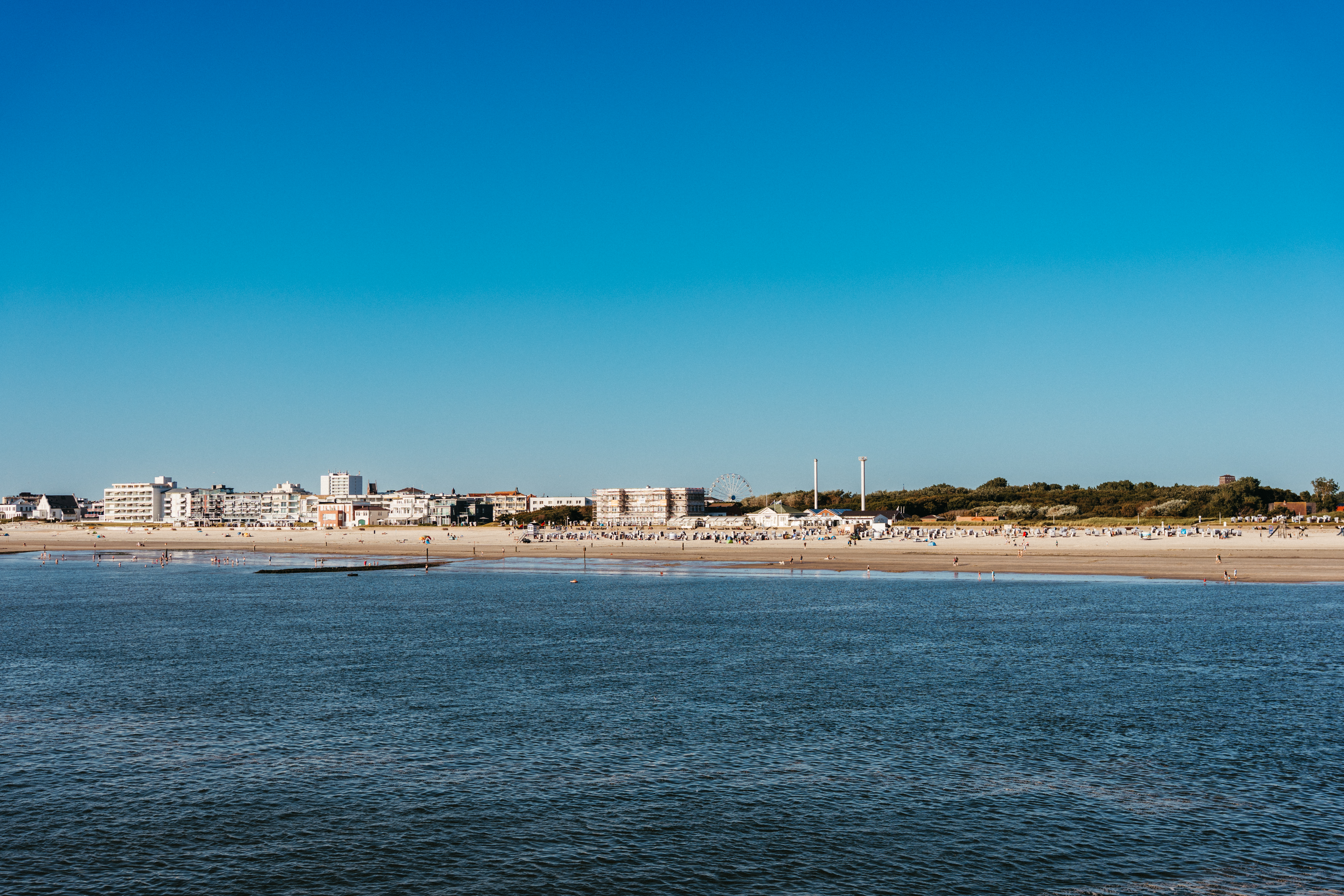 Blick auf einen Sandstrand mit Gebäuden im Hintergrund und blauem Himmel.