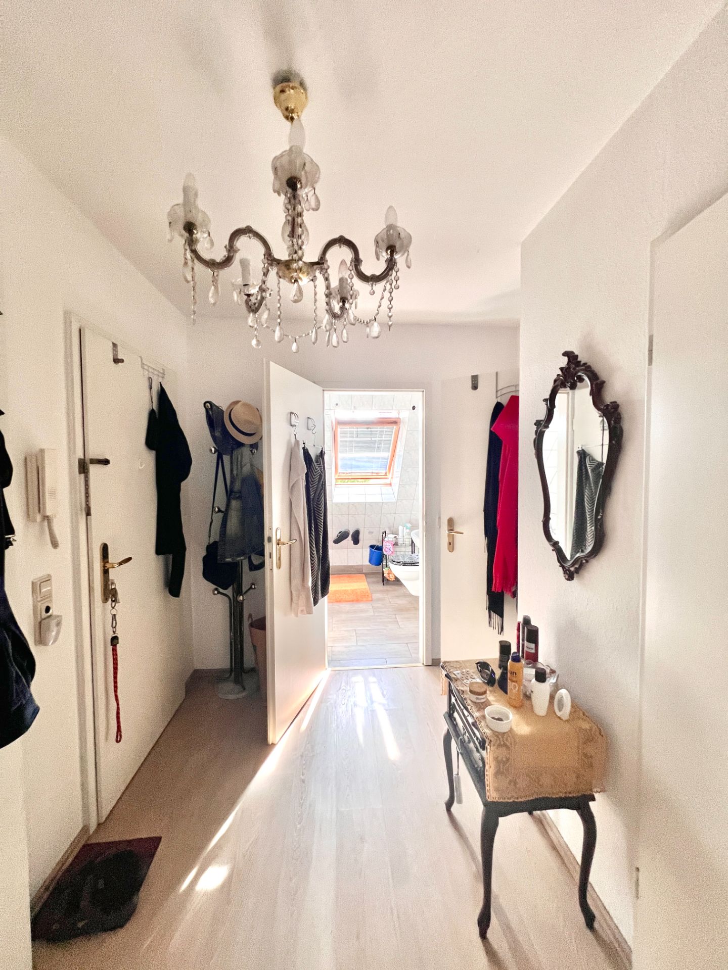 Heller Flur mit Kronleuchter, Spiegel, Kommode und Blick ins Badezimmer.