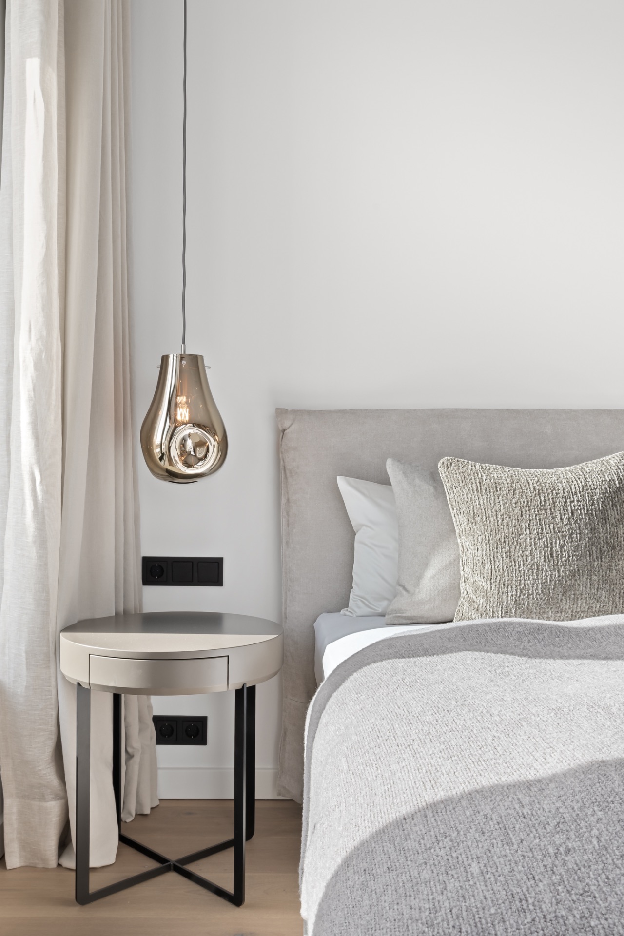 Modernes Schlafzimmer mit rundem Nachttisch, Hängelampe und grauem Bett mit Kissen.