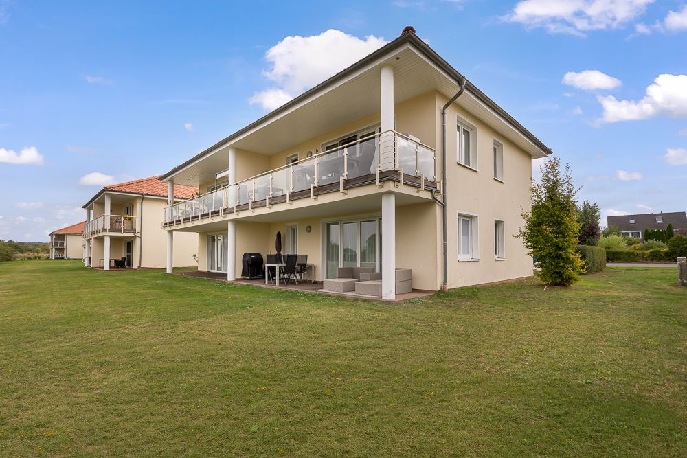 Zweistöckiges Wohnhaus mit Balkon und überdachter Terrasse auf einer großen Rasenfläche.