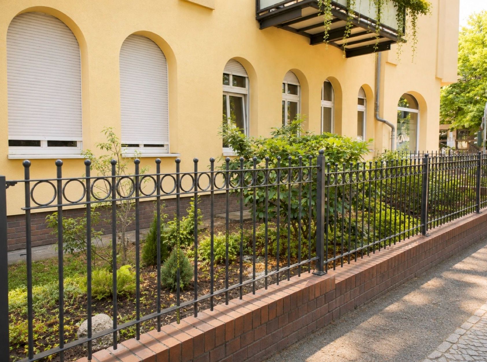 Mehrfamilienhaus mit gelber Fassade, Vorgarten und schwarzem Metallzaun.