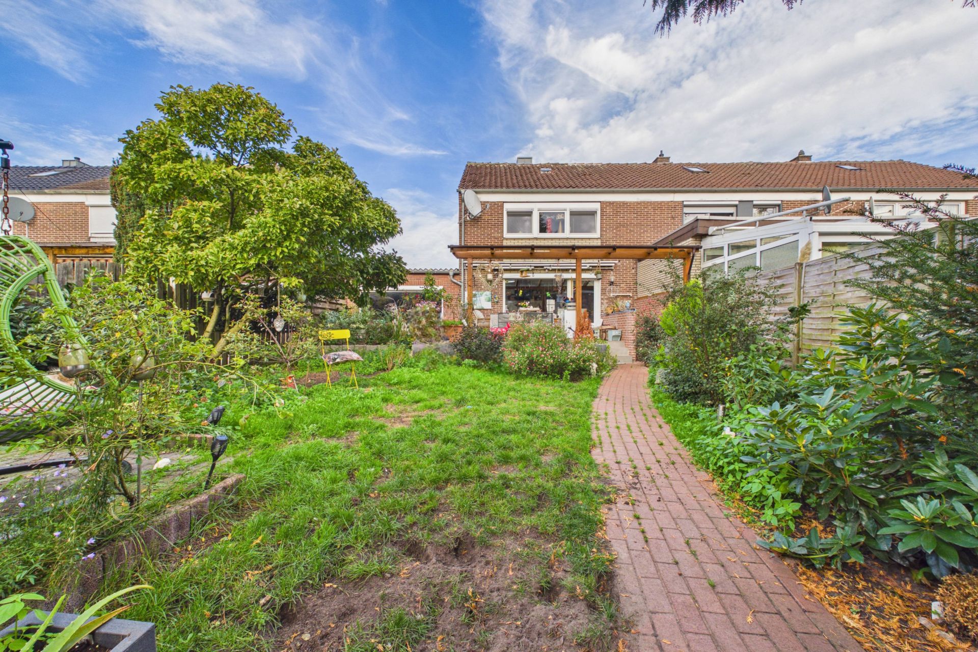 Garten mit Rasen, Bäumen und Gehweg vor einem zweistöckigen Wohnhaus bei Tageslicht.