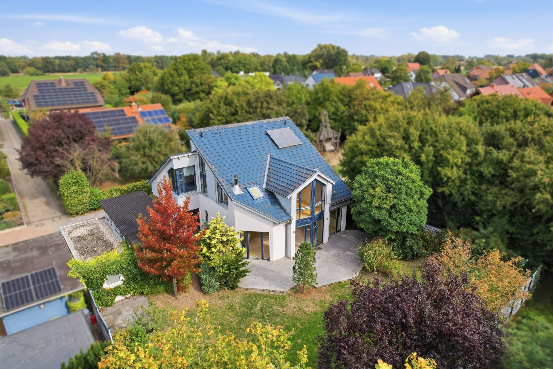 Modernes Einfamilienhaus mit blauem Dach, umgeben von Bäumen und Garten, aus der Vogelperspektive.