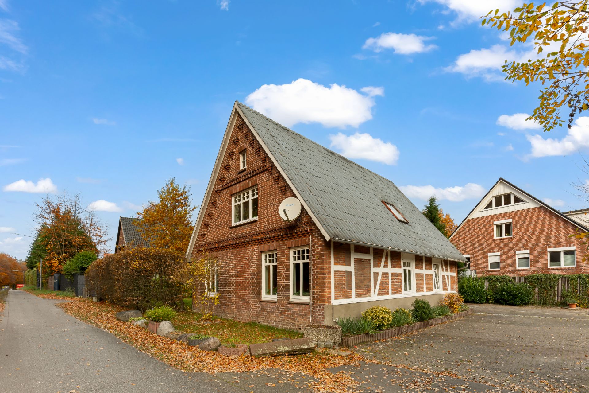 Backsteinhaus mit Satteldach, weißen Fenstern und Vorgarten auf einer ruhigen Straße im Herbst.