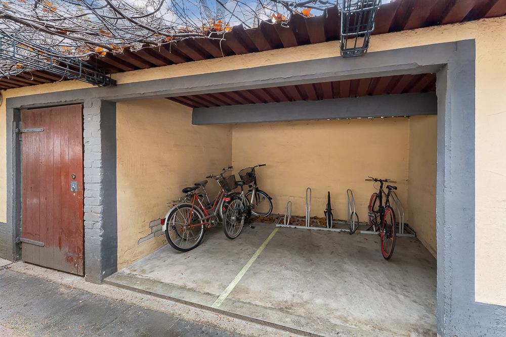 Überdachter Fahrradabstellplatz mit mehreren Fahrrädern und Fahrradständern in einem Innenhof.