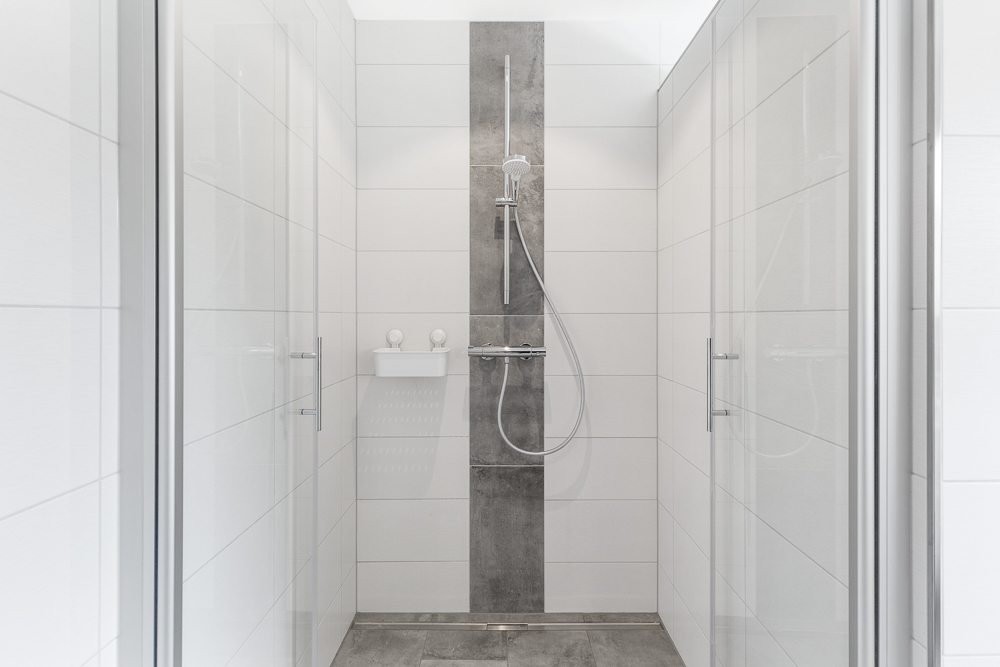 Moderne, geflieste Dusche mit Glastüren und Duschkopf an der Wand.