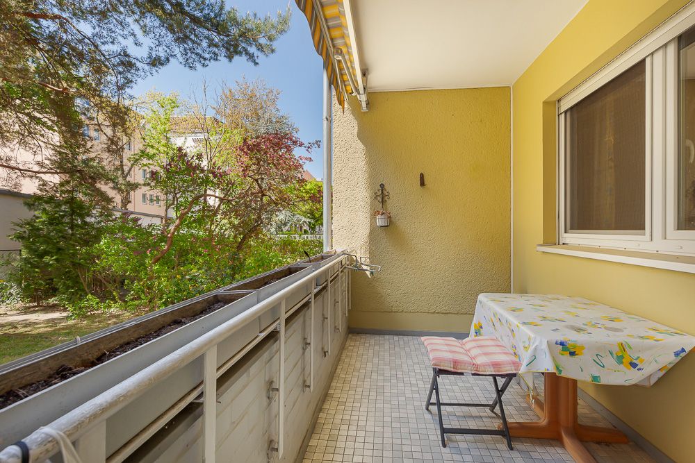 Balkon mit Tisch und Stuhl, Blick ins Grüne, gelbe Hauswand und Markise.