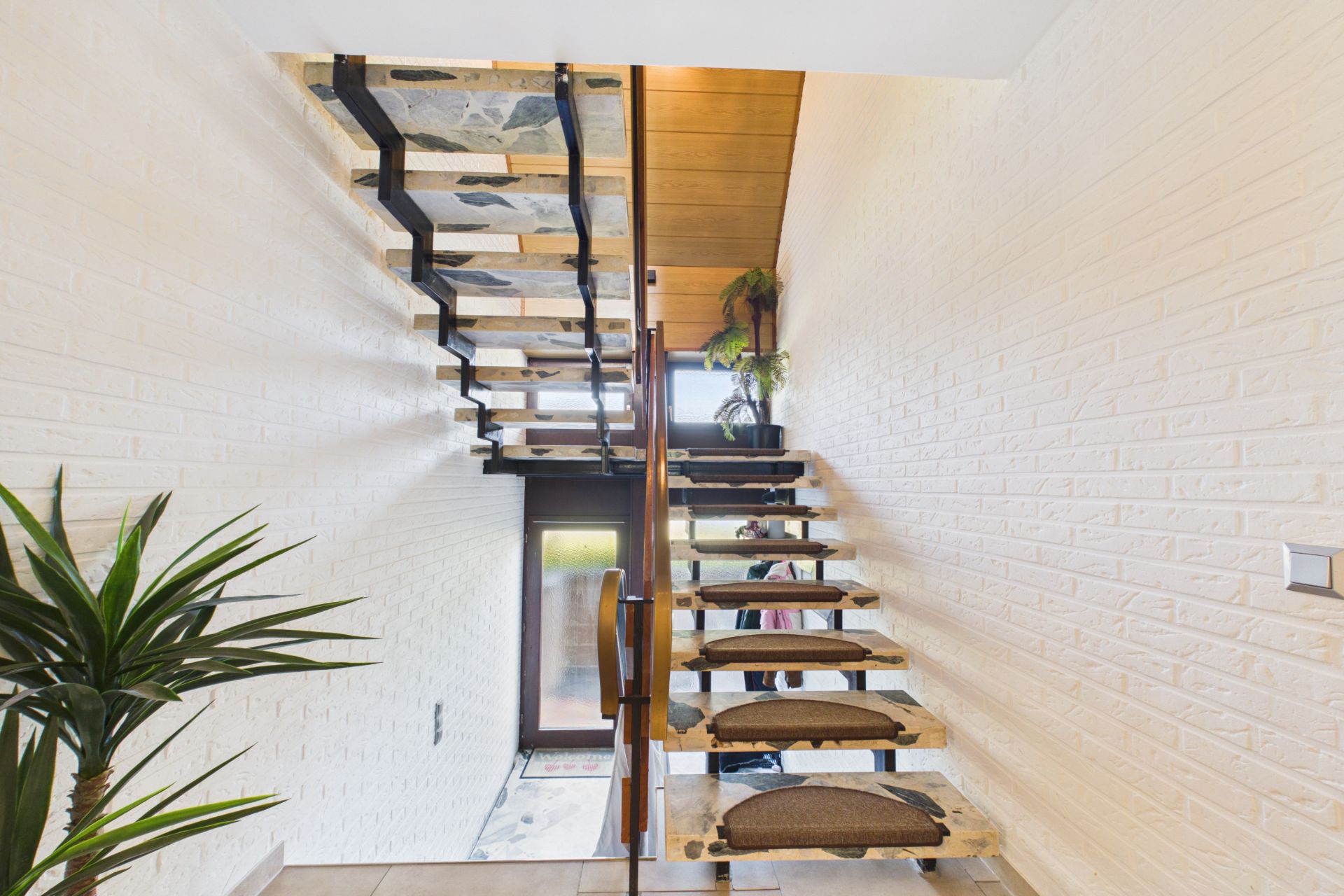 Moderne Treppe mit Holzstufen, weißen Wänden und Pflanzen in einem Wohnhausflur.