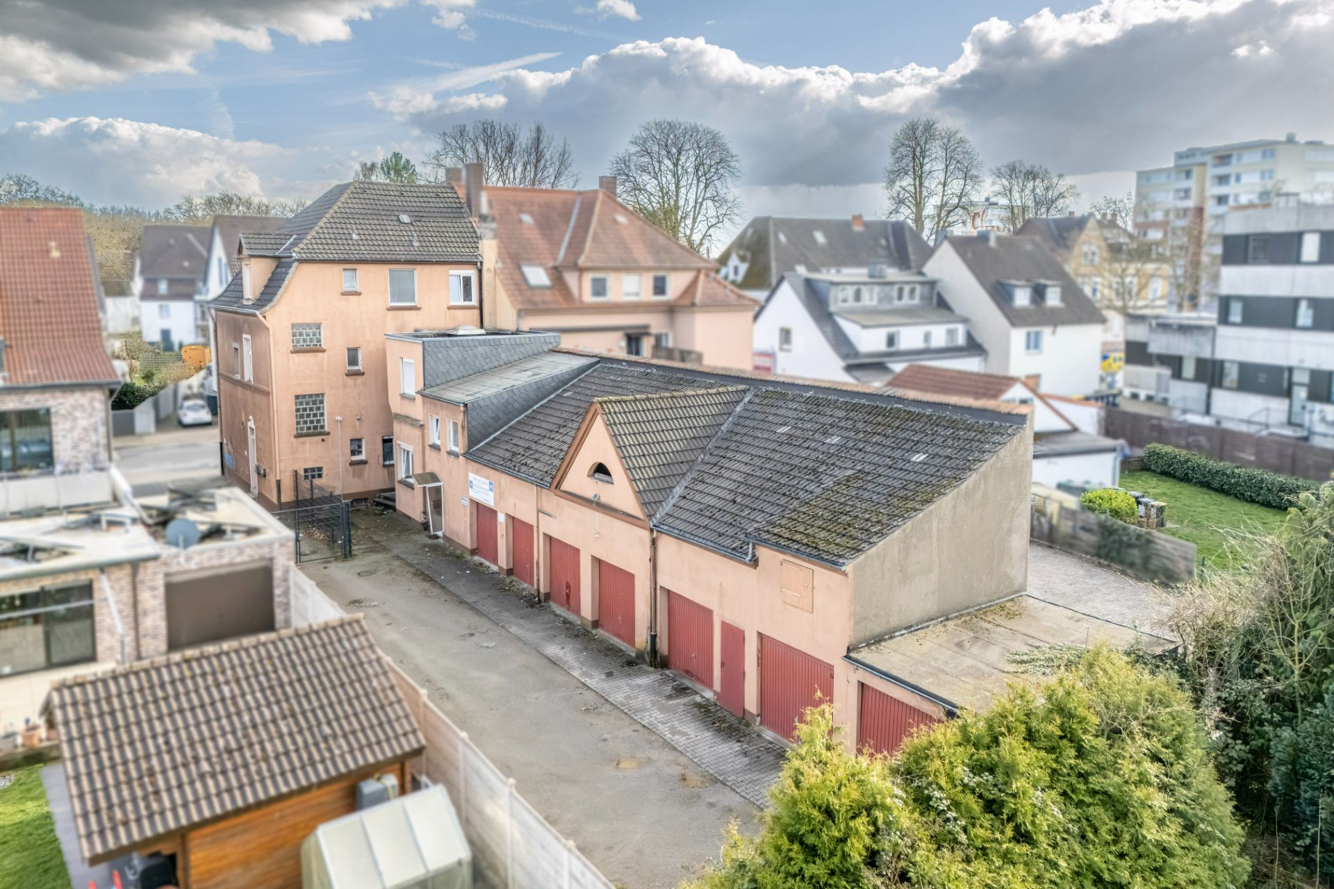 Mehrere Garagen mit roten Toren neben einem Wohnhaus in einer Wohnsiedlung.