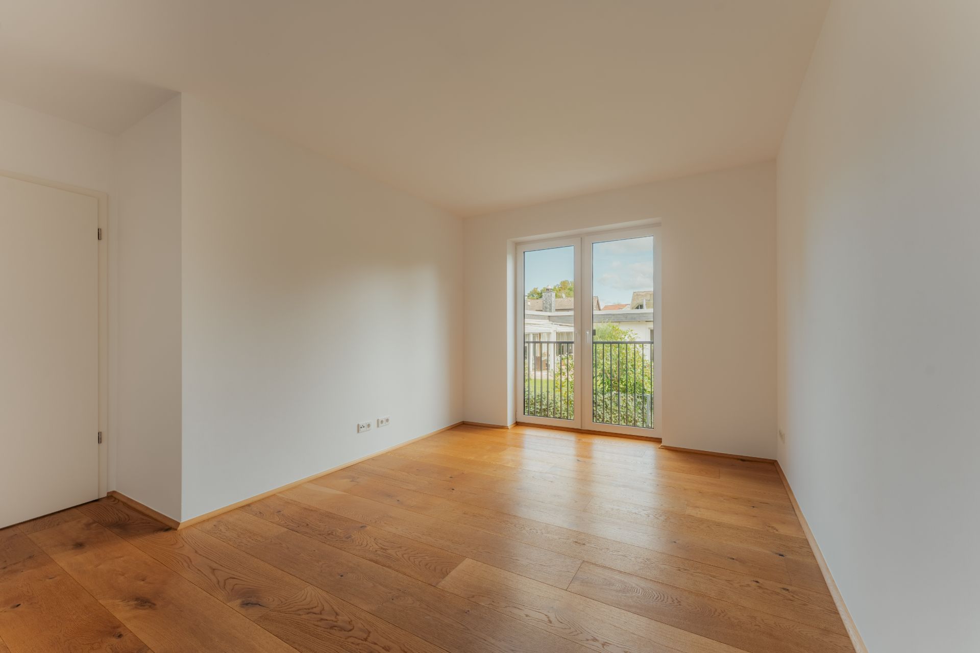 Leerer Raum mit Holzboden, weißen Wänden und Doppelfenster mit Blick nach draußen.