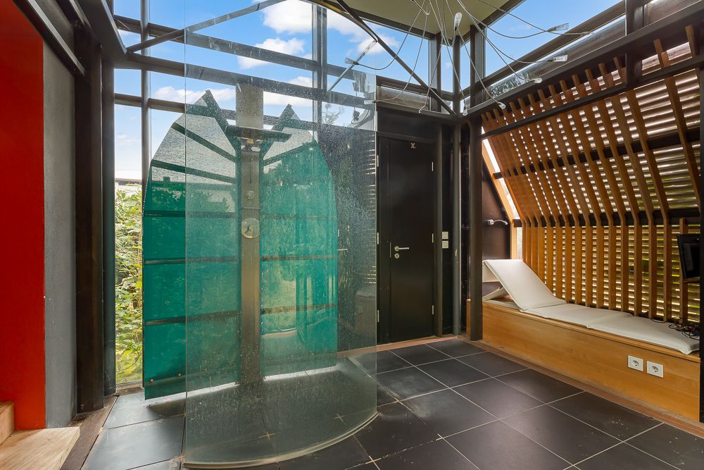 Modernes Badezimmer mit Glasdusche und Liege am Fenster, viel Tageslicht durch große Fenster.