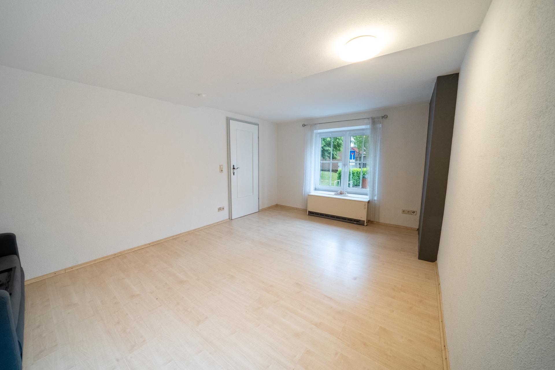 Heller, leerer Raum mit Holzboden, weißer Wand, Fenster und Tür.