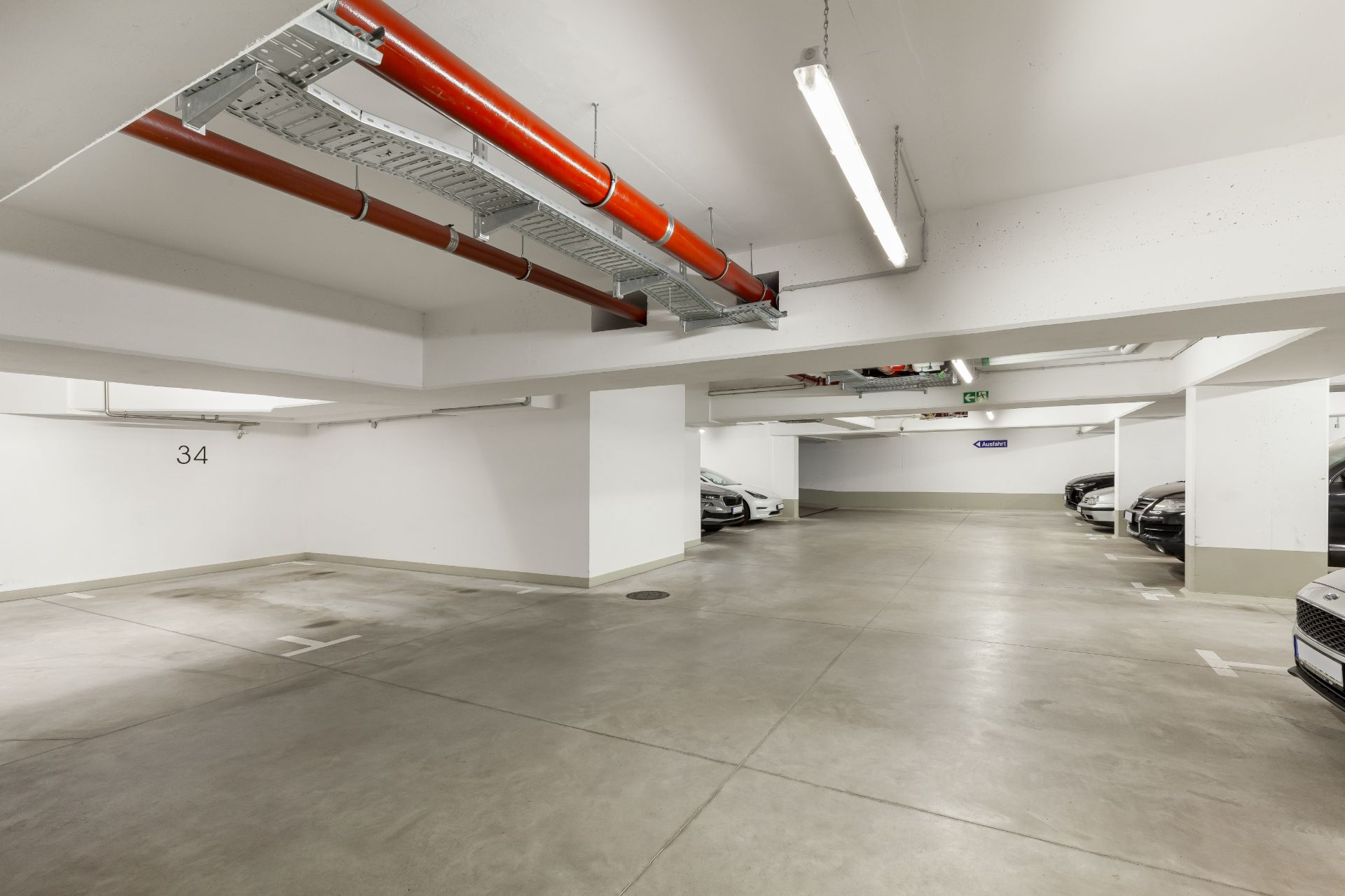 Helle Tiefgarage mit markierten Parkplätzen und geparkten Autos.