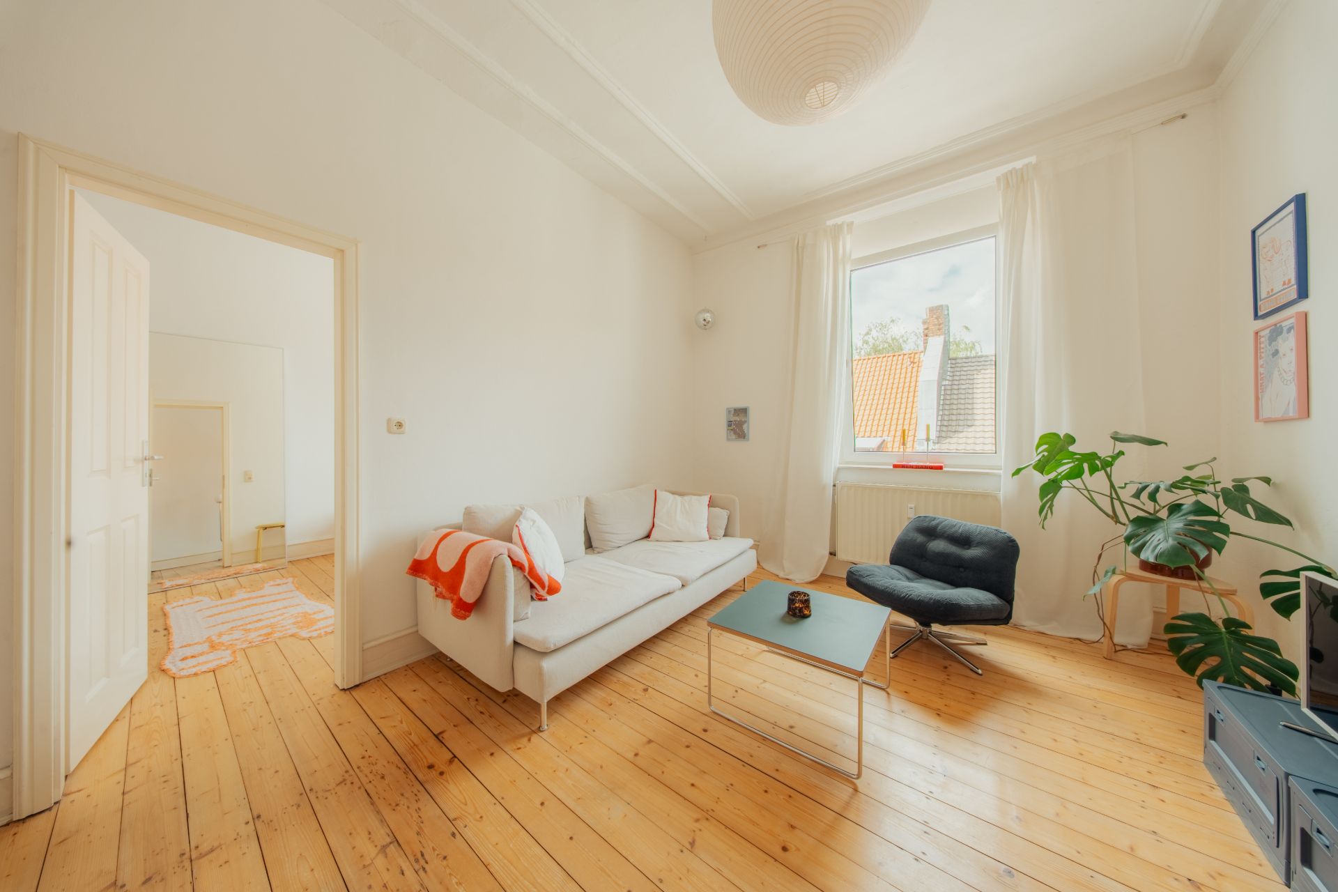 Helles Wohnzimmer mit Sofa, Sessel, Couchtisch und Pflanze auf hellem Holzboden.