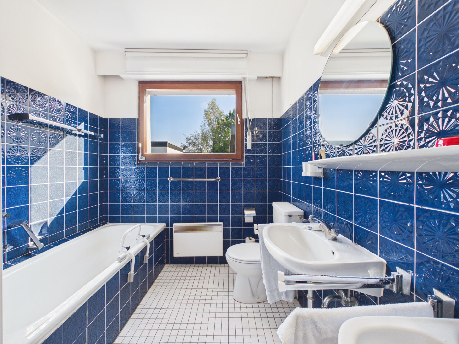 Badezimmer mit blauen Fliesen, Badewanne, Waschbecken, WC und Fenster.