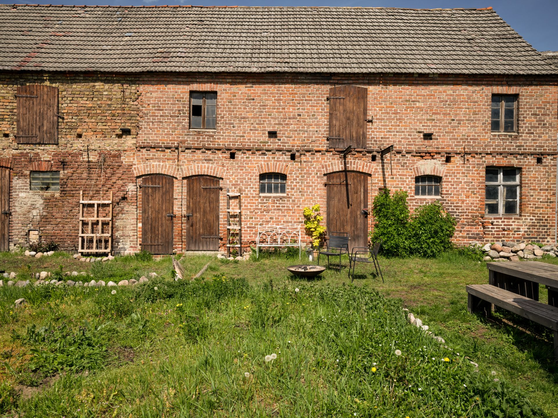 Backsteinfassade eines alten Wohnhauses mit Holztüren und Fenstern, davor ein grasbewachsener Garten.