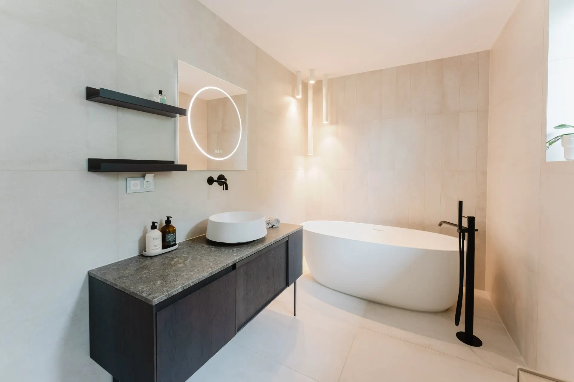 Modernes Badezimmer mit freistehender Badewanne, Waschtisch und beleuchtetem Spiegel.