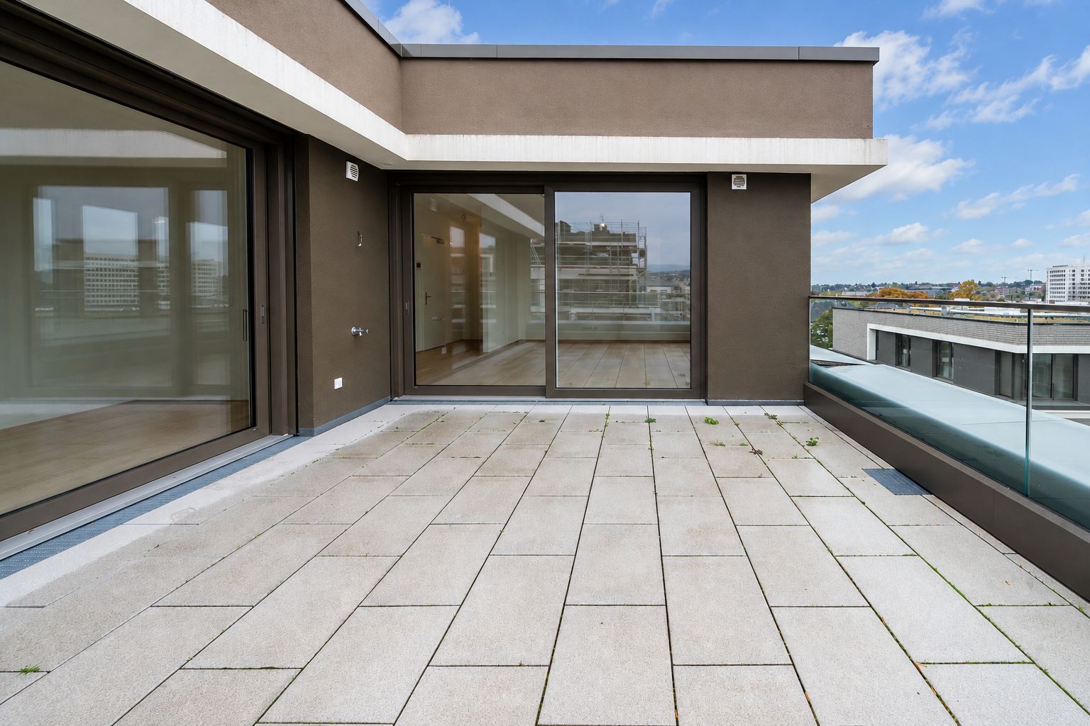 Große Dachterrasse mit Glasgeländer und Zugang zu einem Raum mit großen Fenstern.