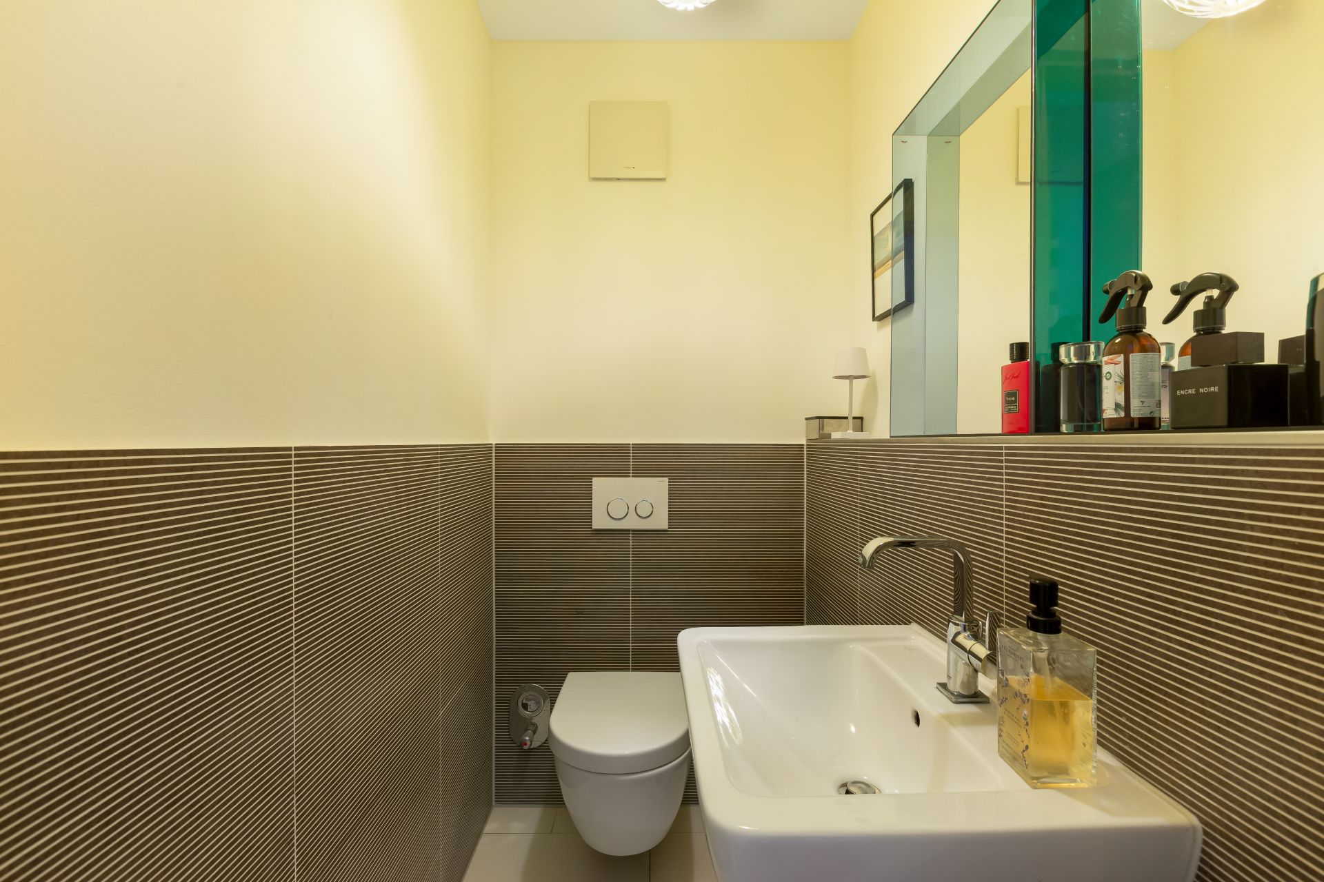 Kleines Badezimmer mit Wandtoilette, Waschbecken und Spiegel, Fliesen an den Wänden.