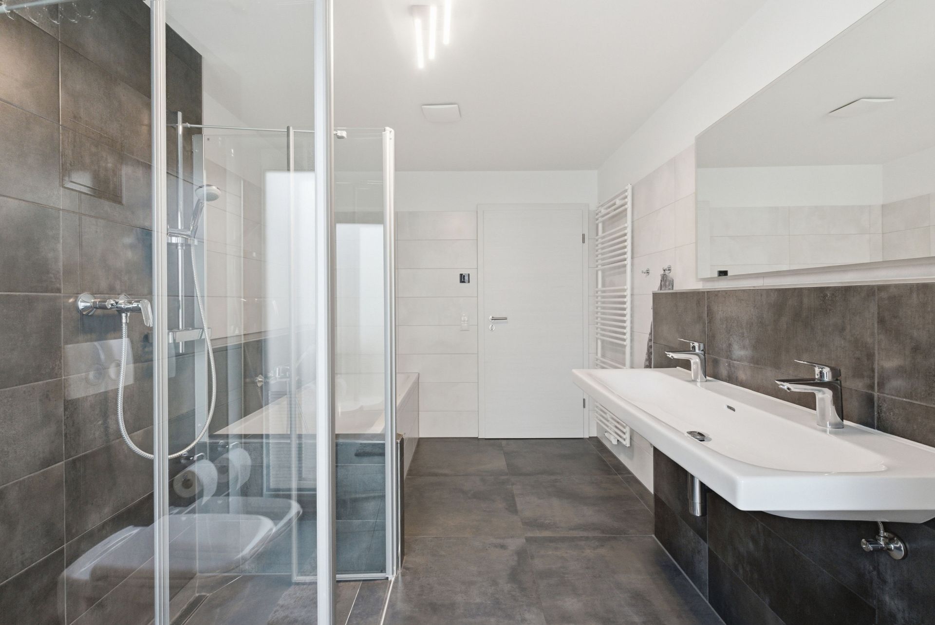 Modernes Badezimmer mit Dusche, Doppelwaschbecken, Spiegel und Handtuchheizkörper.