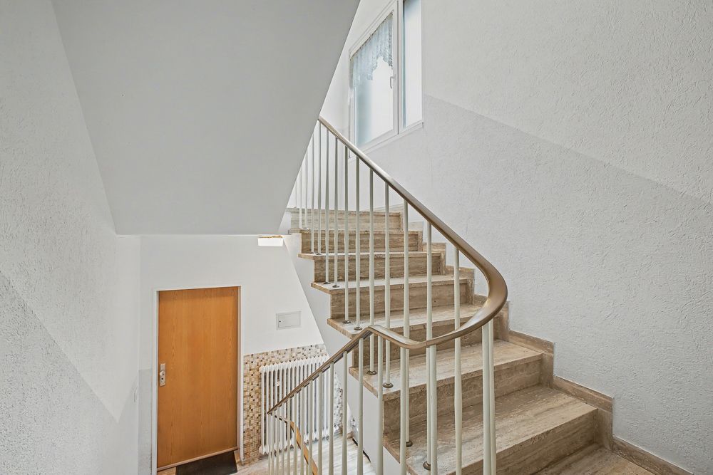 Innenansicht eines Treppenhauses mit braunen Stufen, Geländer und Fenster.