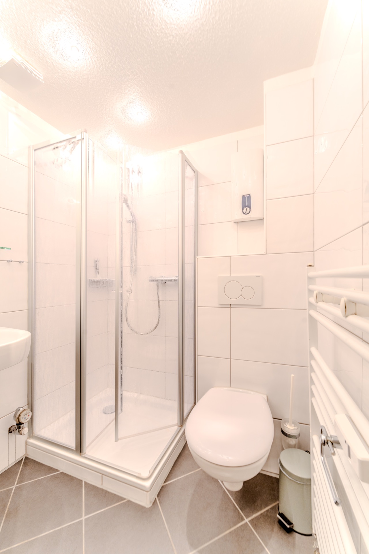 Kleines, modernes Badezimmer mit Dusche, WC, Waschbecken und Handtuchheizkörper.