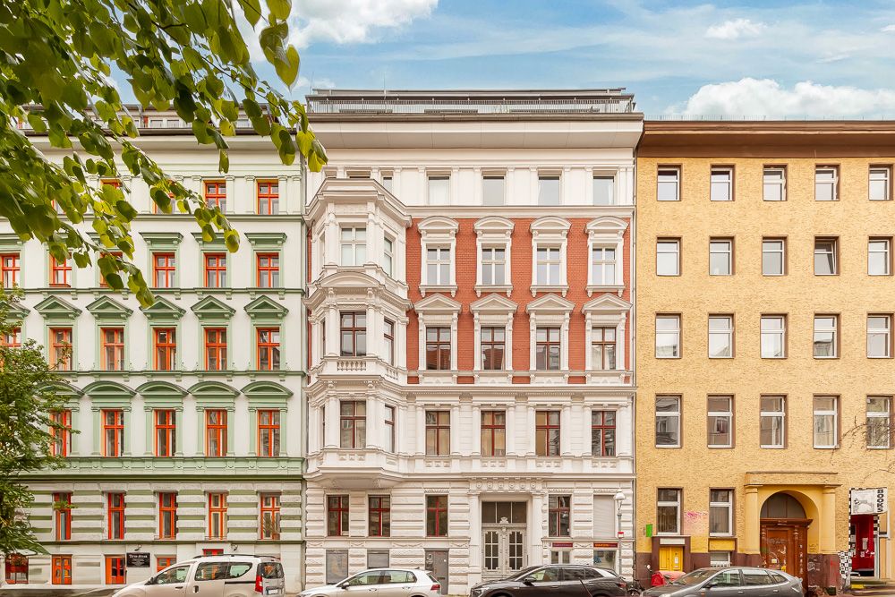 Mehrstöckiges Wohnhaus mit historischer Fassade, Autos parken davor.