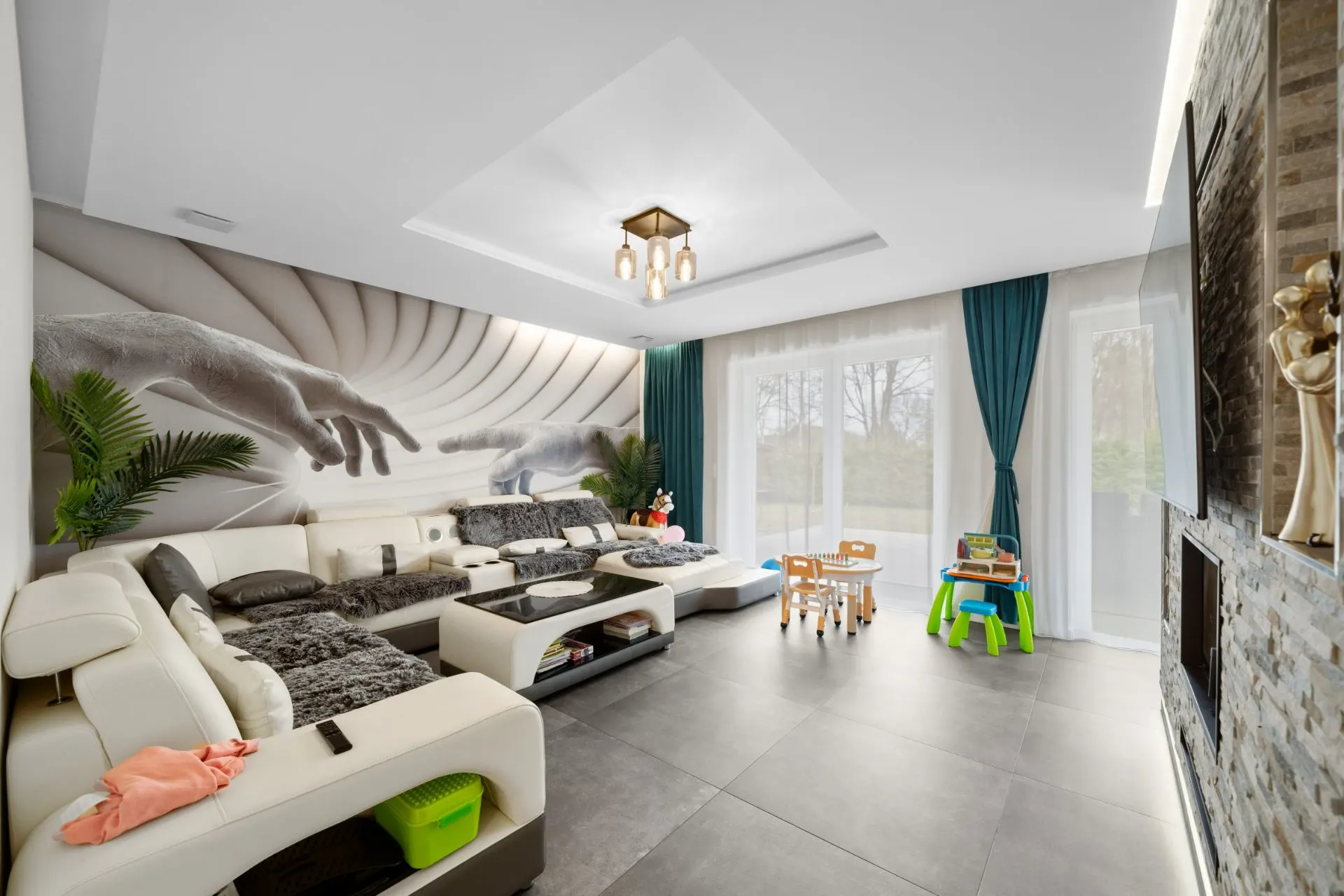 Modernes Wohnzimmer mit großer Sofaecke, Wandmalerei, Spieltisch und großen Fenstern.