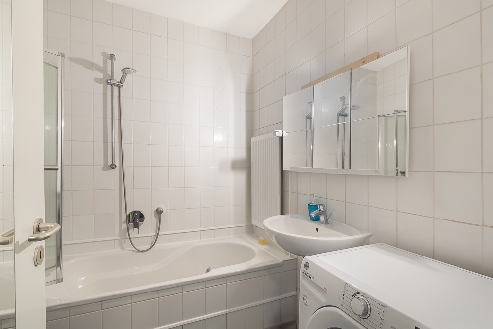 Helles Badezimmer mit Badewanne, Waschbecken, Spiegel und Waschmaschine.