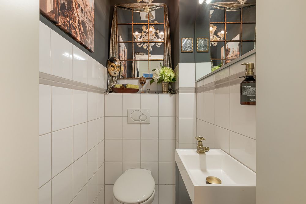 Kleines WC mit weiß gefliesten Wänden, kleinem Waschbecken und Dekoration über der Toilette.