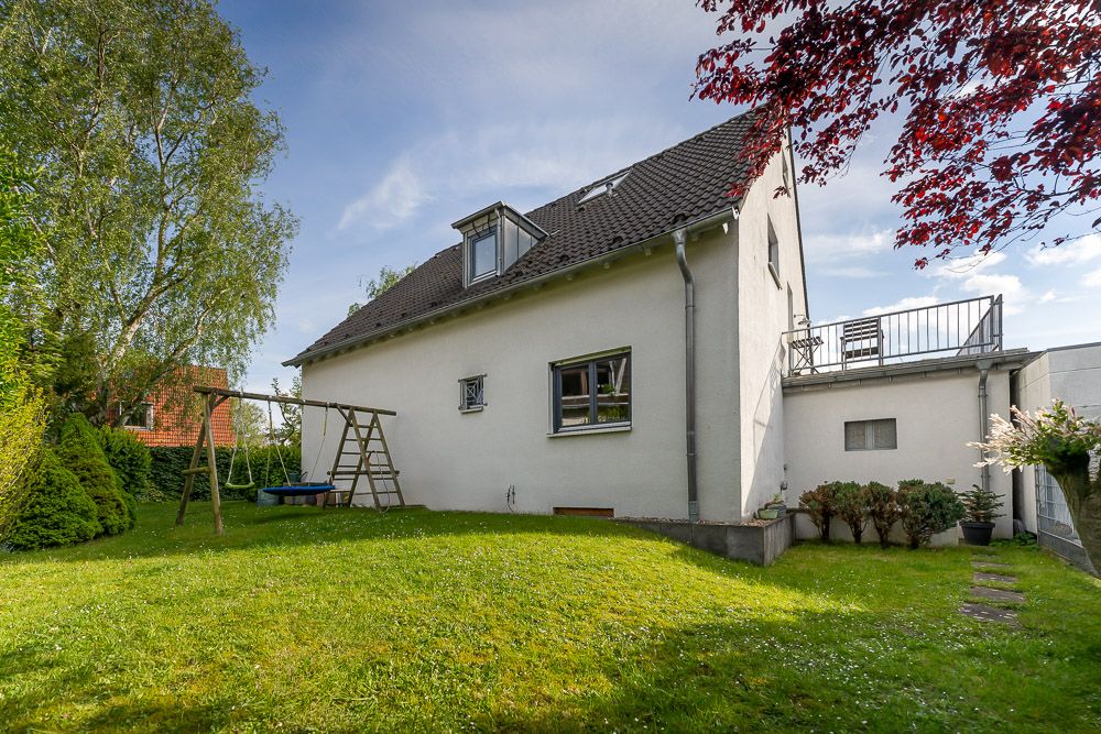 Weißes Einfamilienhaus mit Schaukeln im Garten, grüne Wiese und Bäume.