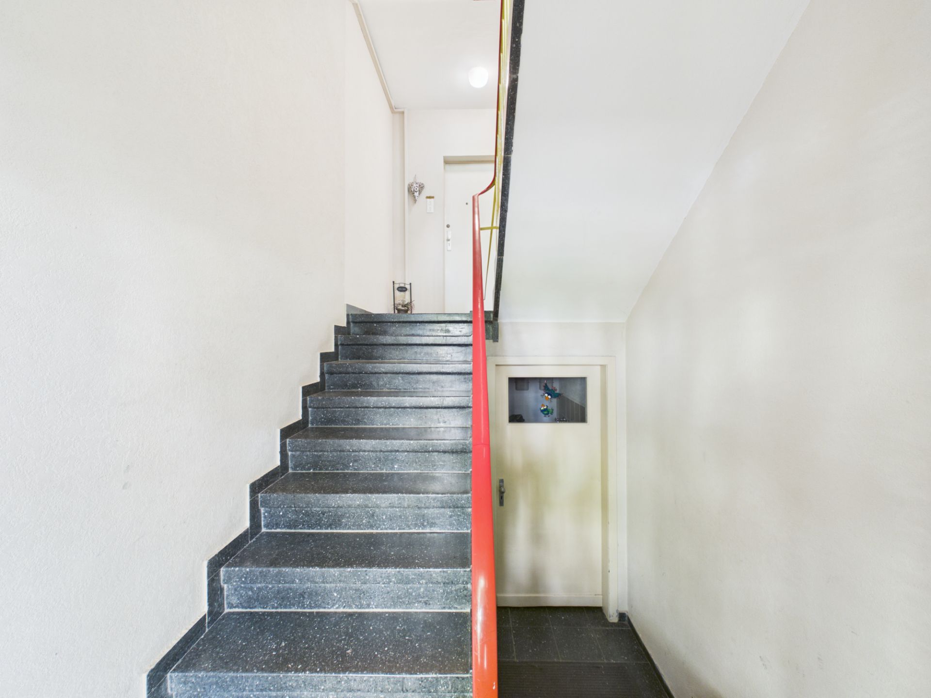 Treppe mit schwarzem Stufen und rotem Geländer in einem hellen Flur.