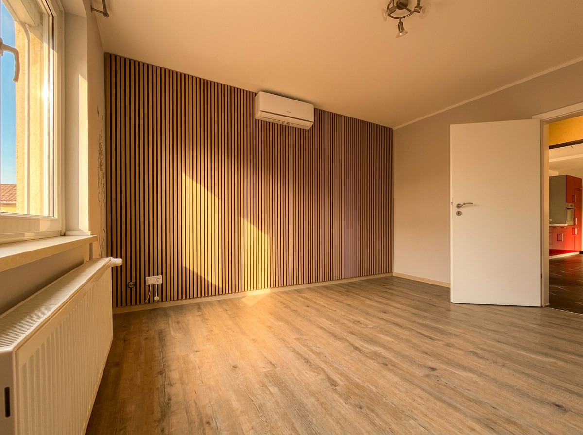 Leeres Zimmer mit Holzfußboden, Fenster, Heizung und Holzverkleidung an einer Wand.