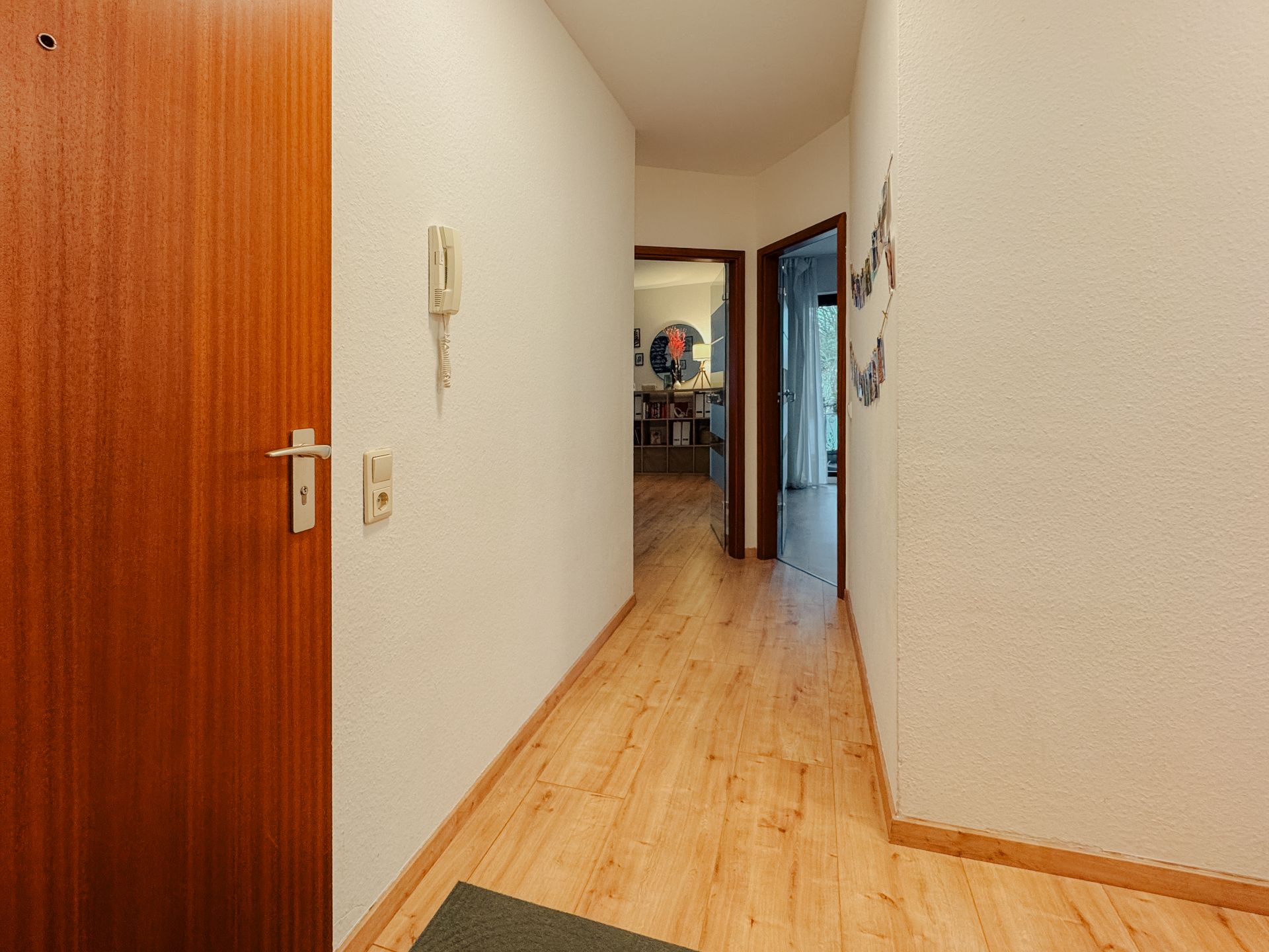 Flur mit Holzboden, weißen Wänden und offener Tür zu weiteren Zimmern in einer Wohnung.