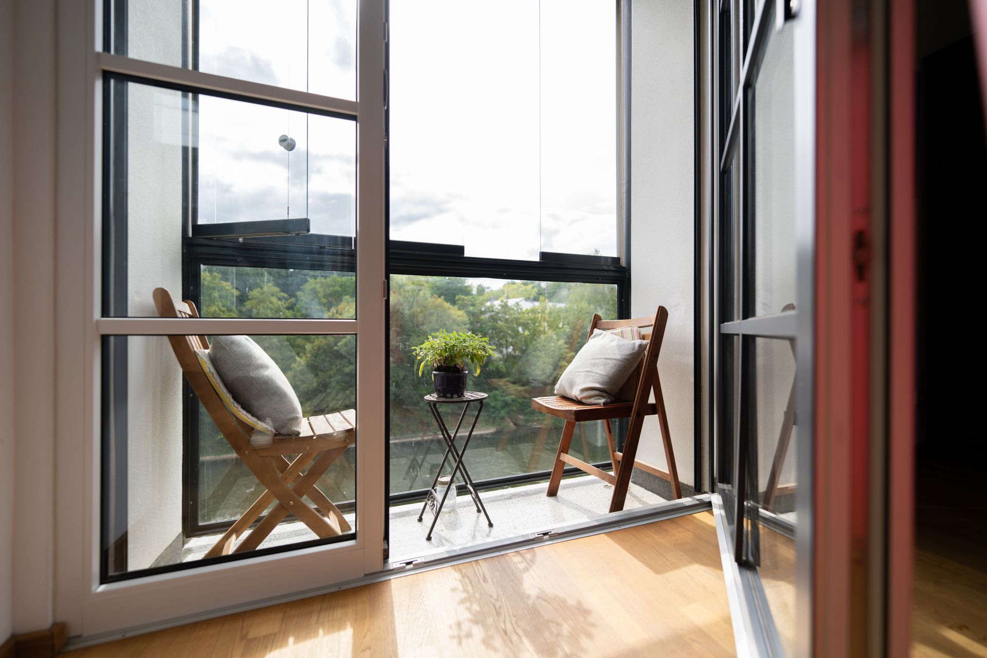 Kleiner Balkon mit zwei Holzstühlen, Kissen und einem Tisch mit Pflanze, Blick ins Grüne.