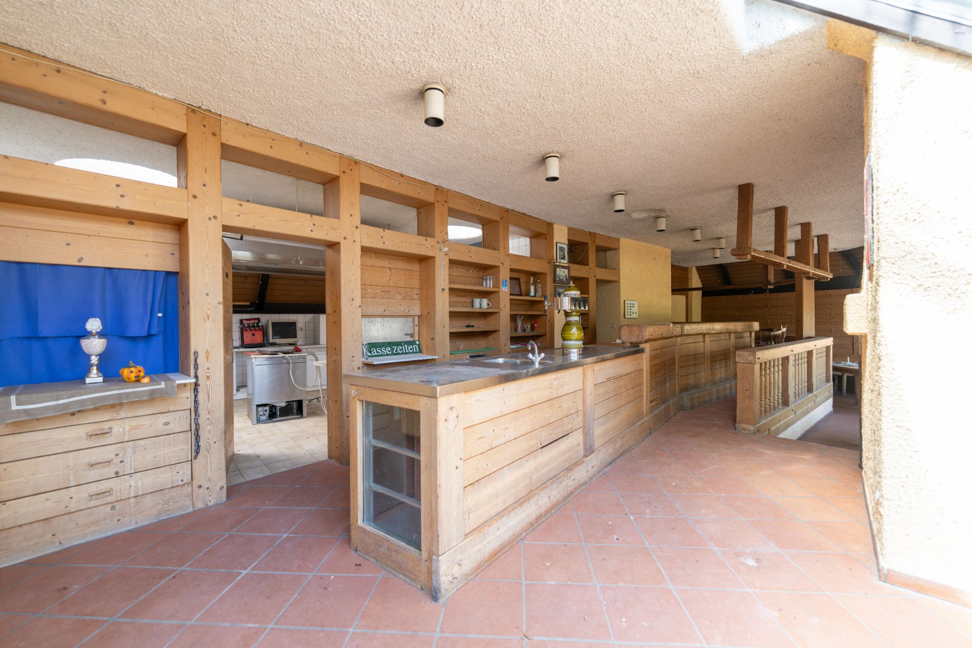 Offene Küche mit langer Holztheke, Regalen und Fliesenboden.