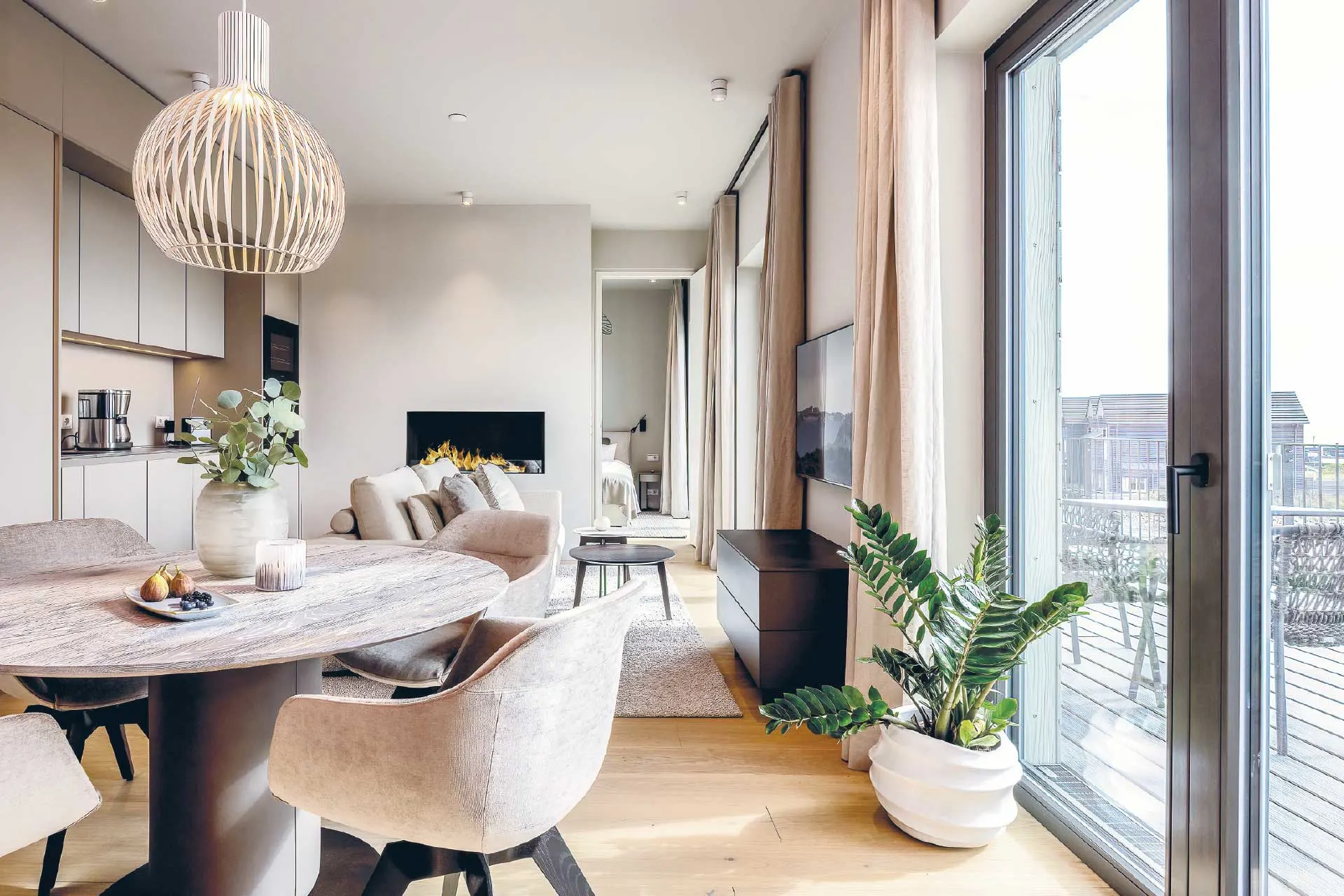 Heller Wohn- und Essbereich mit Esstisch, Sesseln, Sofa, Pflanze und Zugang zum Balkon.