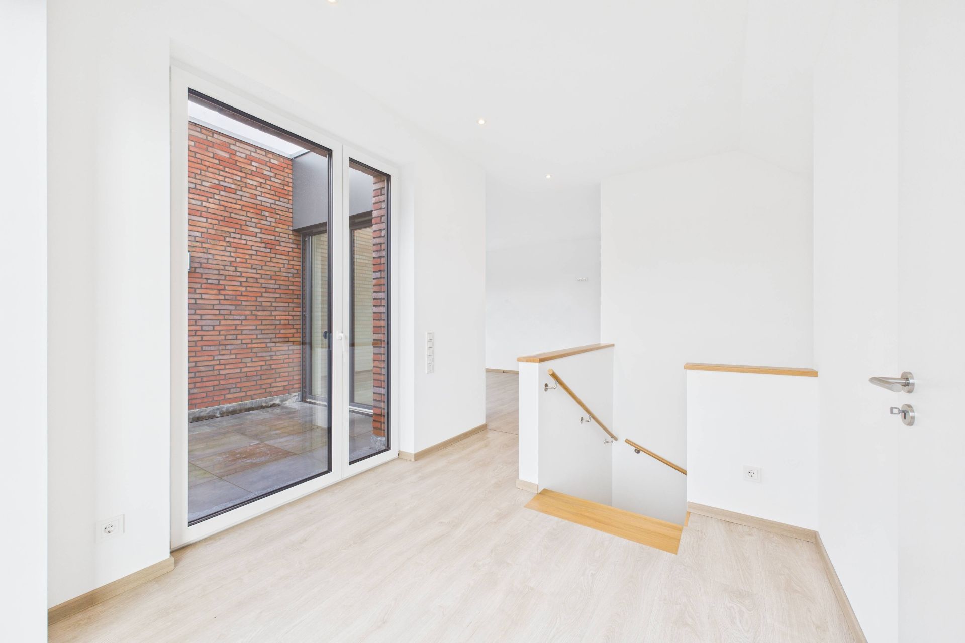 Heller Flur mit Glastür zu Terrasse und Treppe mit Holzgeländer.