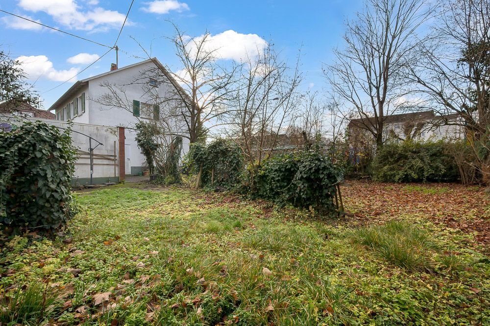 Haus mit weißer Fassade und grünem Garten, umgeben von Bäumen und Sträuchern.