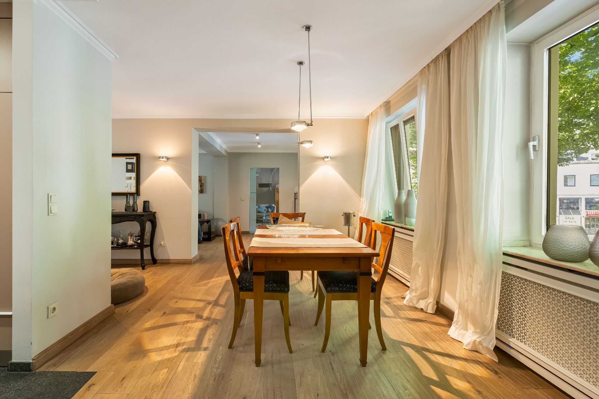 Esszimmer mit Holzfußboden, großem Holztisch, sechs Stühlen und großen Fenstern mit Vorhängen.