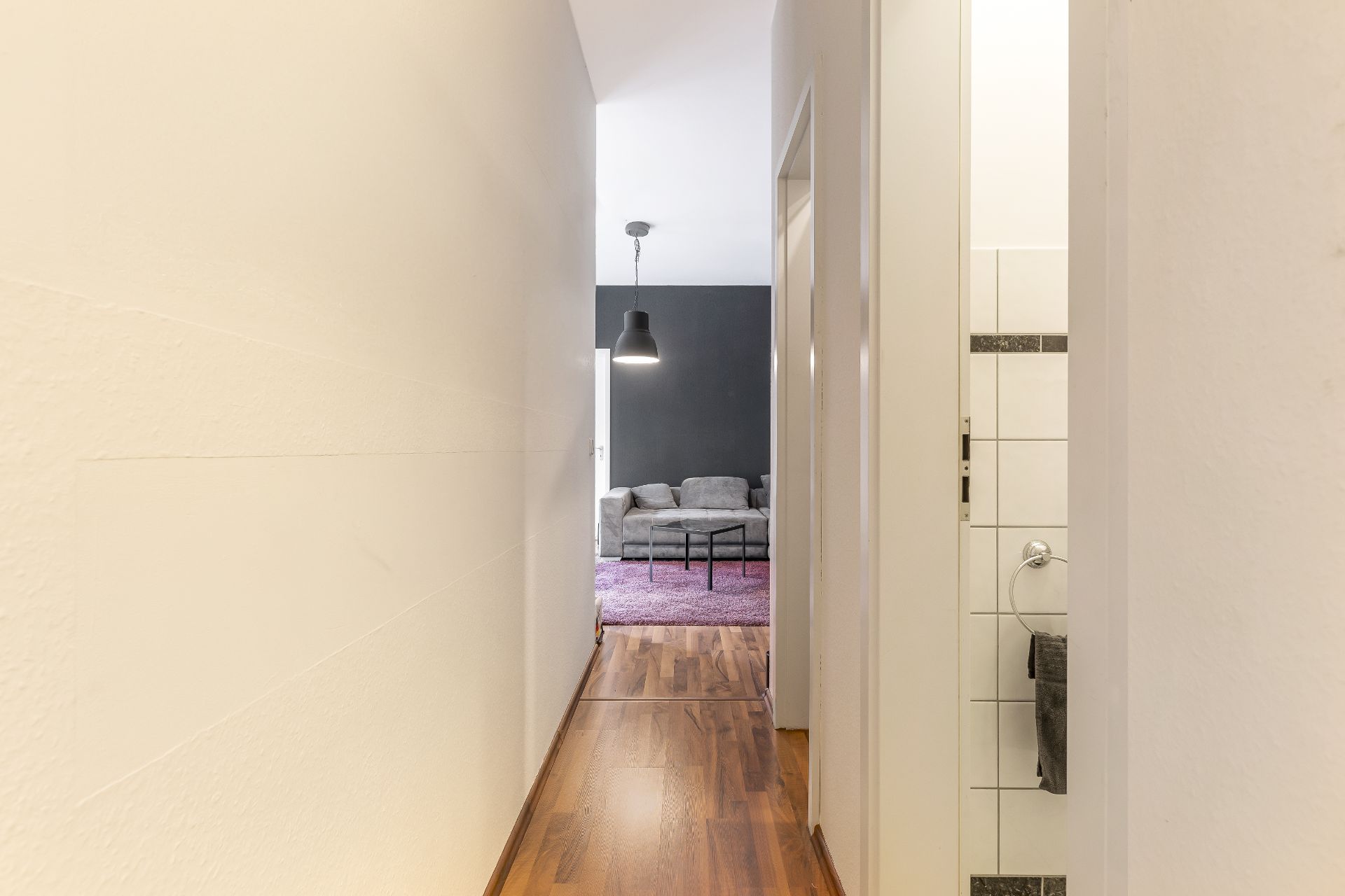 Heller Flur mit Holzboden, Blick auf ein Wohnzimmer mit grauem Sofa und schwarzer Lampe.
