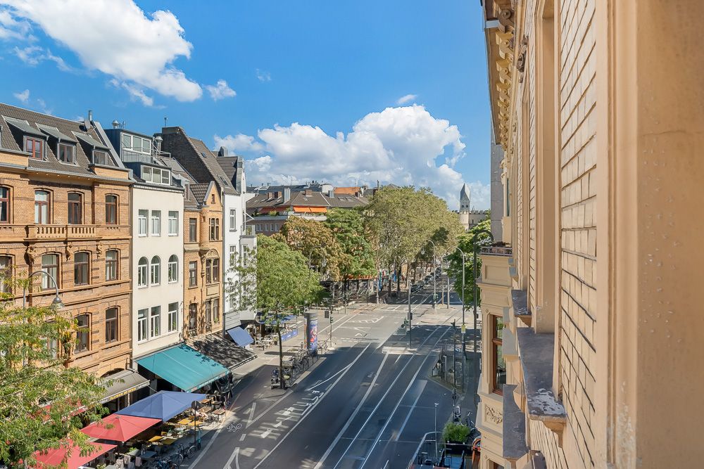 Blick von einem Balkon auf eine breite Straße mit Altbauten, Bäumen und Straßencafés.