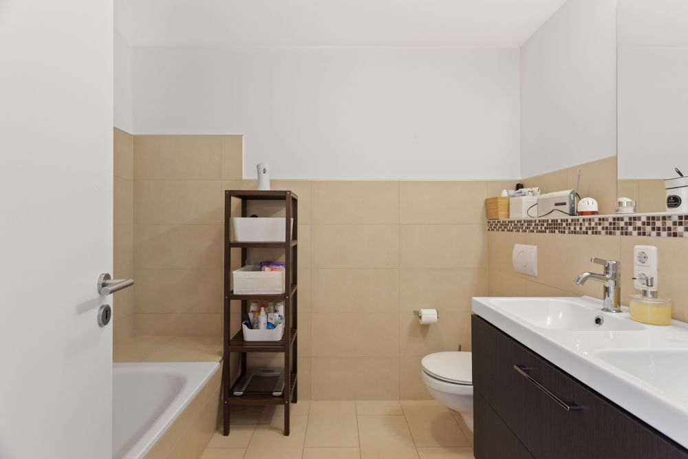 Modernes Badezimmer mit Badewanne, Regal, Toilette und Waschbecken mit Spiegel.