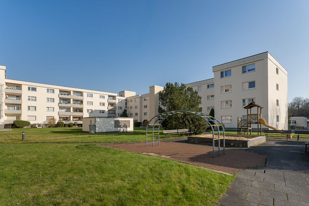 Mehrfamilienhäuser mit Spielplatz, Rutsche und Klettergerüst im grünen Innenhof.