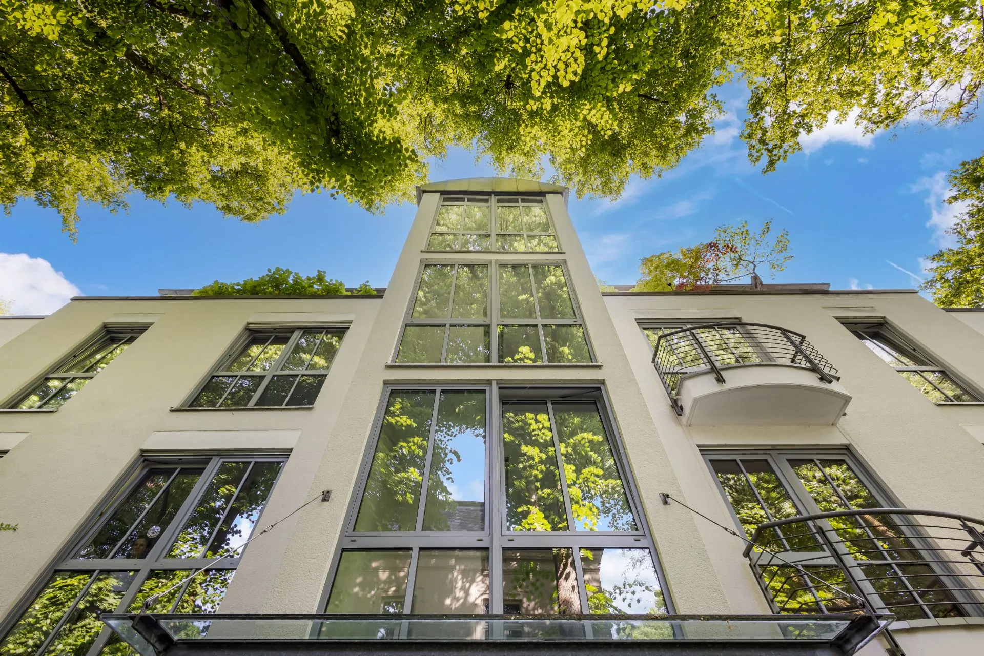 Moderne Wohnhausfassade mit großen Fenstern und Balkonen, von unten fotografiert.