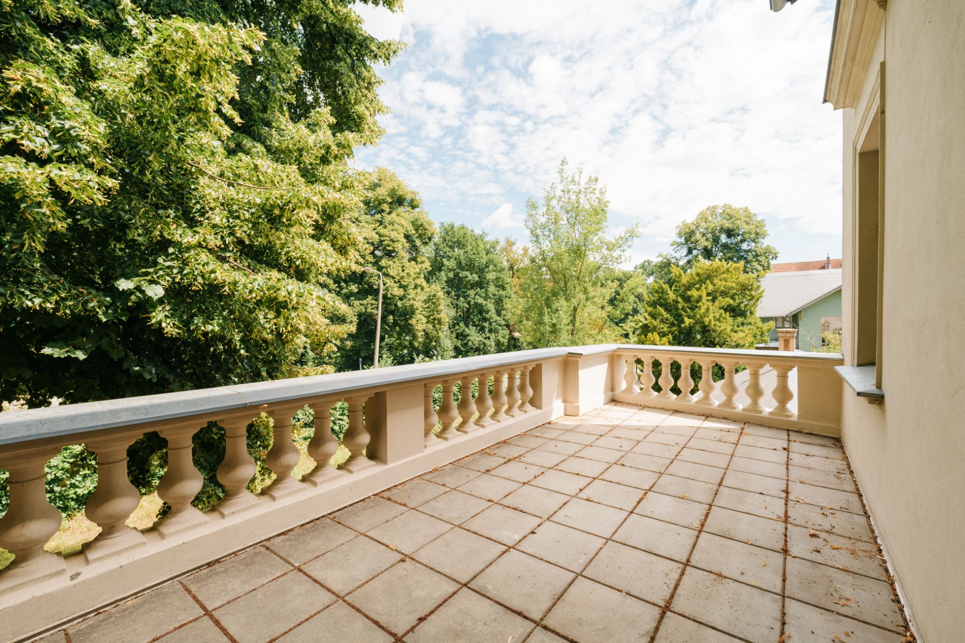 Große Terrasse mit Steinboden und Balustrade, umgeben von grünen Bäumen.