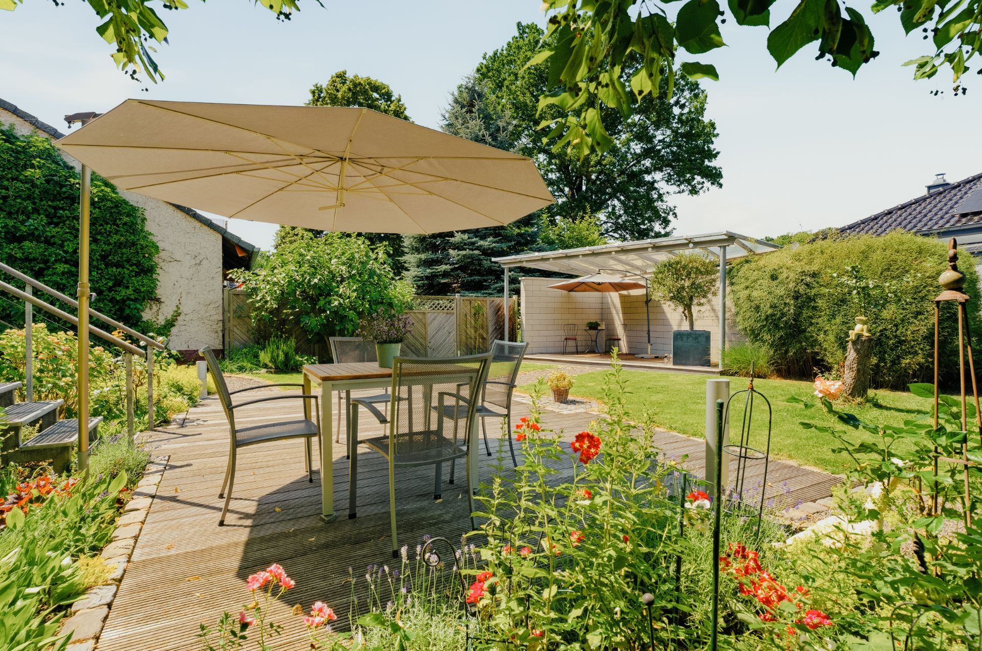 Terrasse mit Tisch, Stühlen und Sonnenschirm im blühenden Garten eines Wohnhauses.