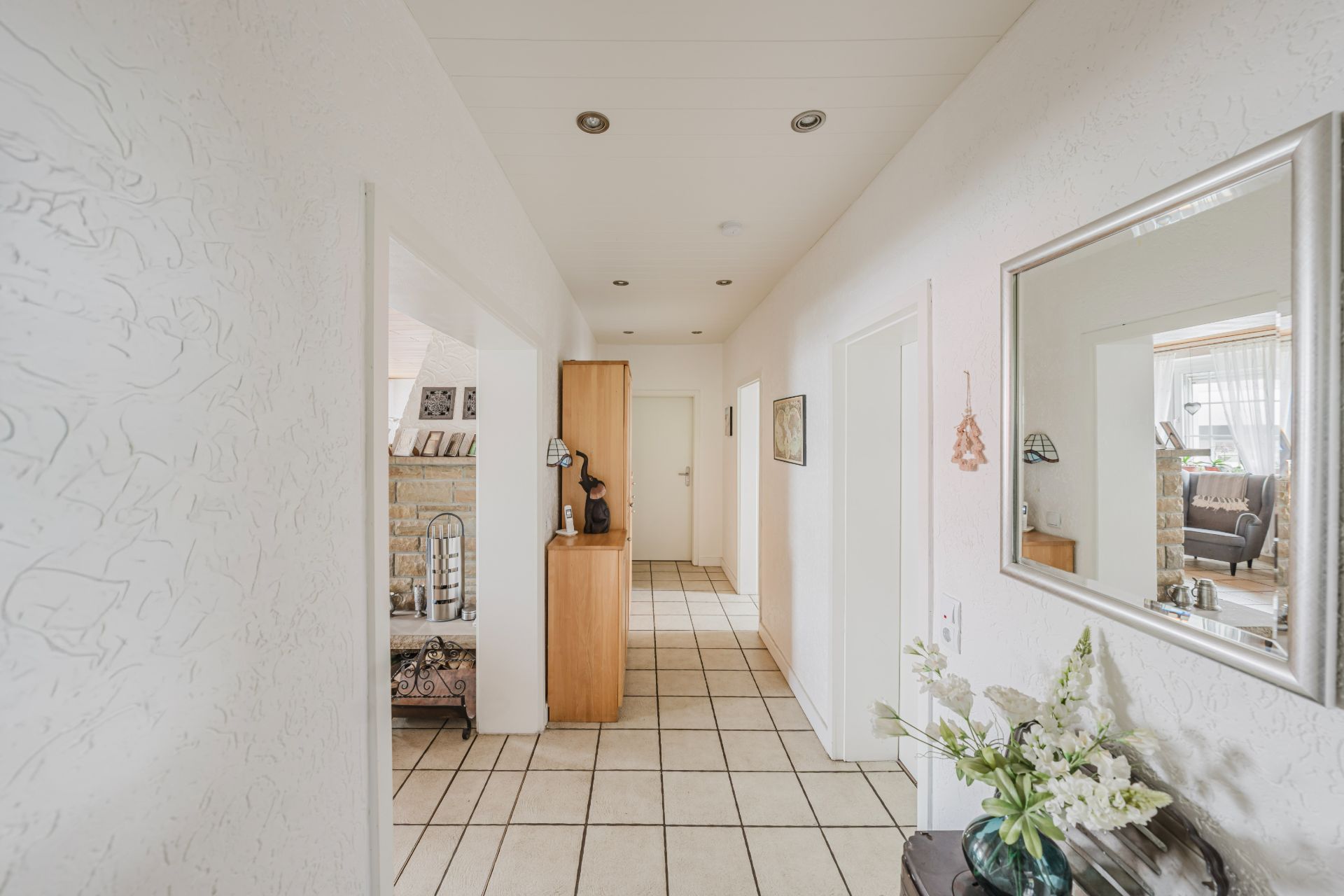 Heller Flur mit Fliesenboden, Spiegel an der Wand und Blumen auf einer Kommode.