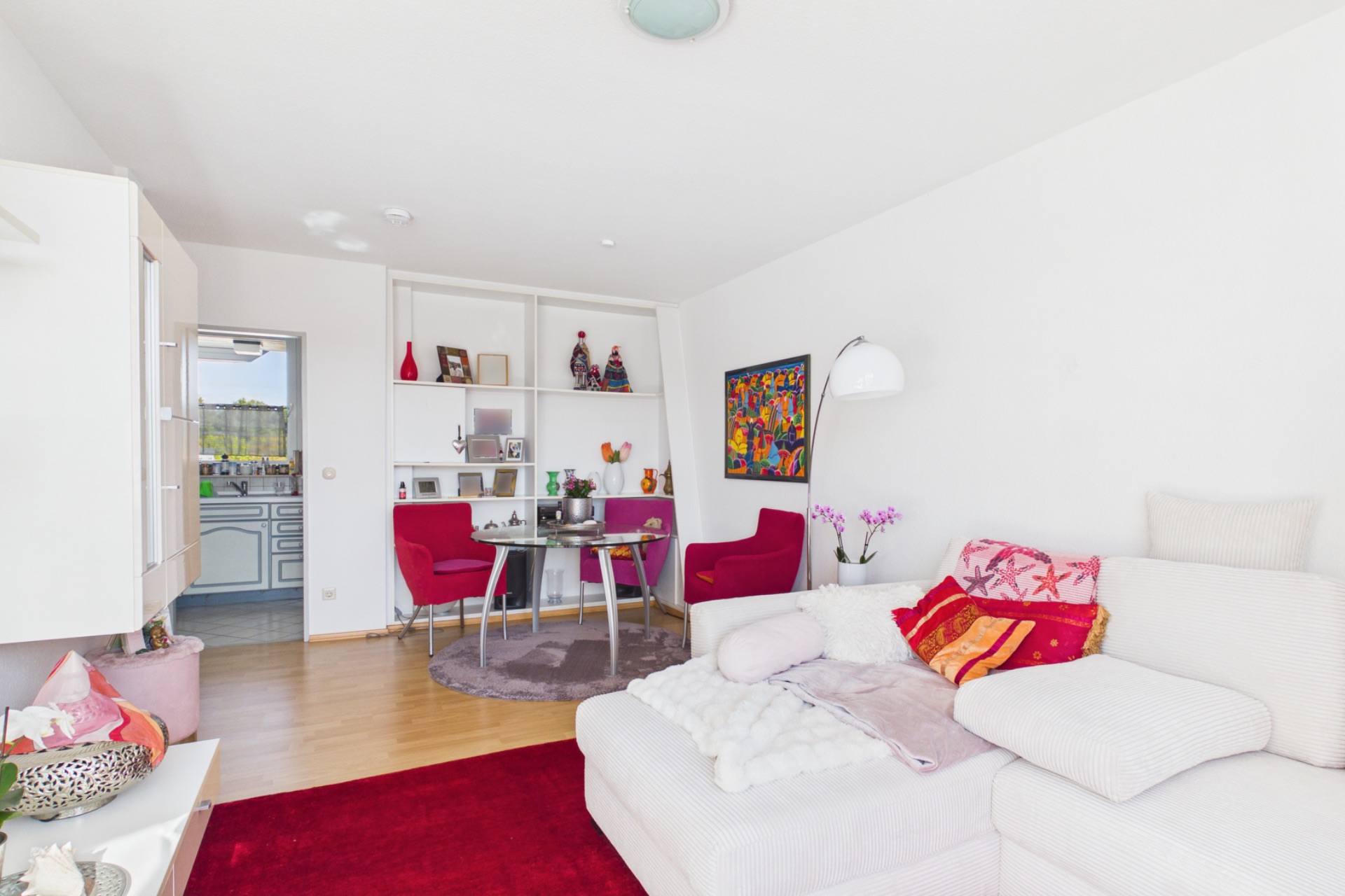 Helles Wohnzimmer mit weißem Sofa, roten Sesseln, Esstisch und Dekorelementen.