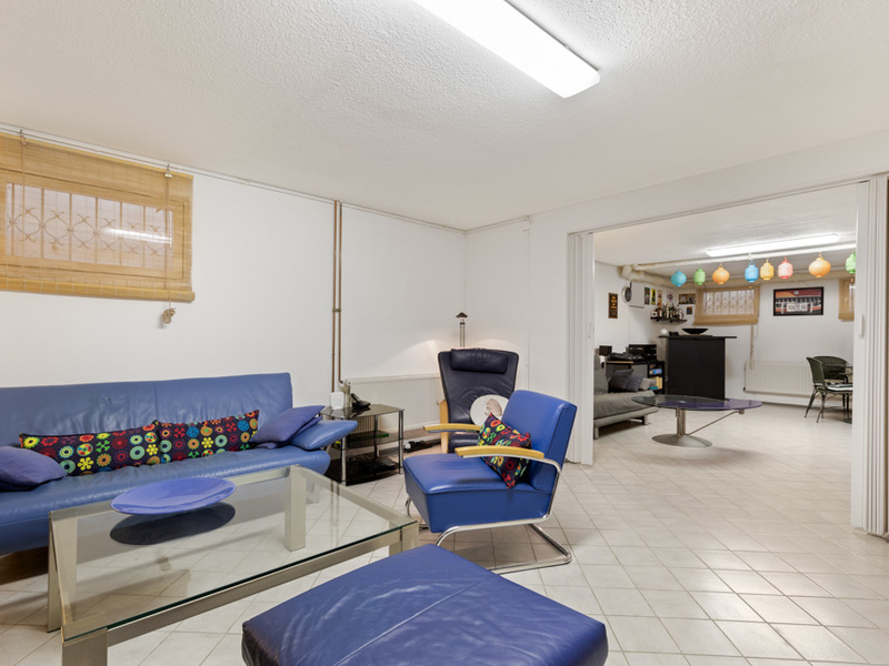 Wohnzimmer mit blauen Möbeln, Glastisch und Blick in einen weiteren Raum mit bunten Lampions.